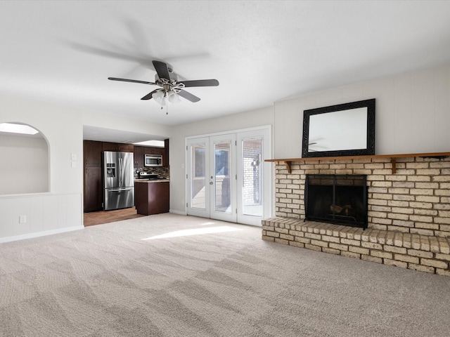 unfurnished living room with a ceiling fan, a fireplace, light colored carpet, and french doors