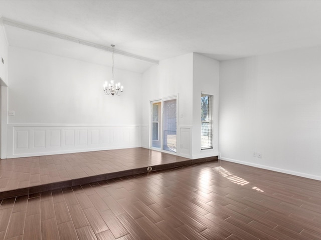 unfurnished room featuring a notable chandelier, a wainscoted wall, lofted ceiling, and wood finished floors