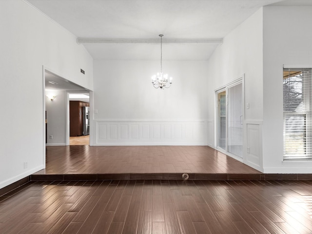 unfurnished room with wood finished floors, baseboards, a towering ceiling, wainscoting, and a chandelier