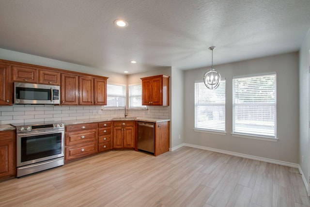 kitchen with a sink, stainless steel appliances, brown cabinets, backsplash, and a chandelier