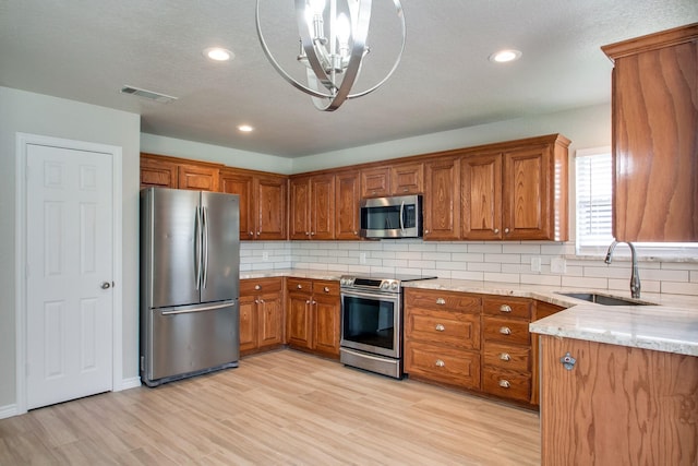 kitchen featuring light wood finished floors, decorative backsplash, brown cabinets, stainless steel appliances, and a sink