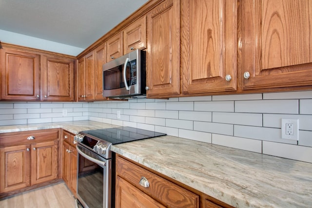 kitchen with stainless steel appliances, light stone countertops, decorative backsplash, and brown cabinetry