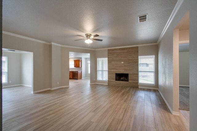 unfurnished living room with light wood finished floors, visible vents, a tiled fireplace, ornamental molding, and a ceiling fan