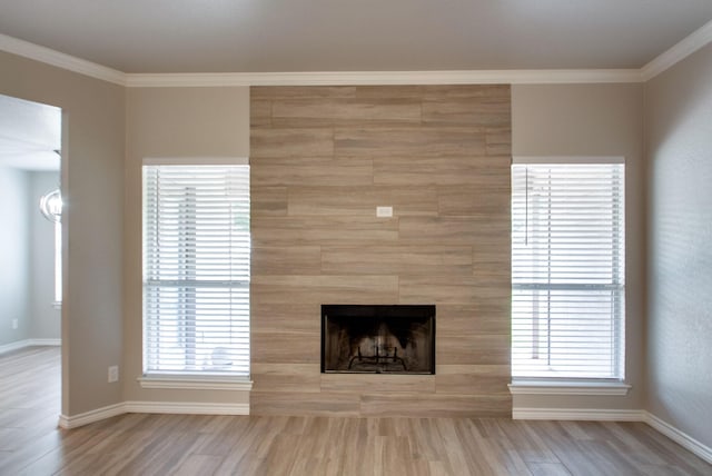 unfurnished living room with a tiled fireplace, crown molding, wood finished floors, and baseboards