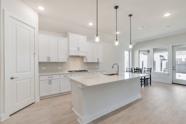 kitchen featuring a kitchen island with sink, a sink, under cabinet range hood, backsplash, and stainless steel gas cooktop