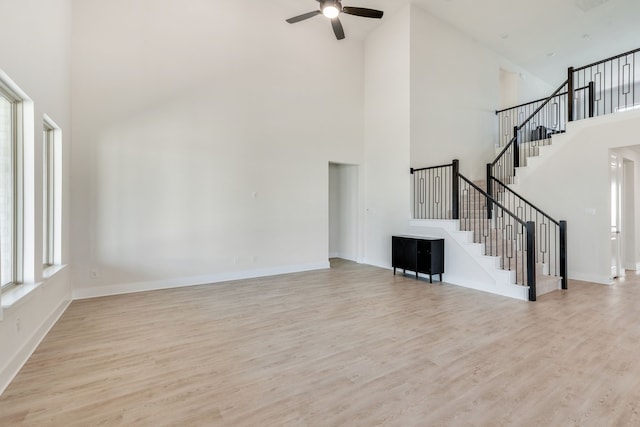 unfurnished living room featuring ceiling fan, stairway, baseboards, and wood finished floors