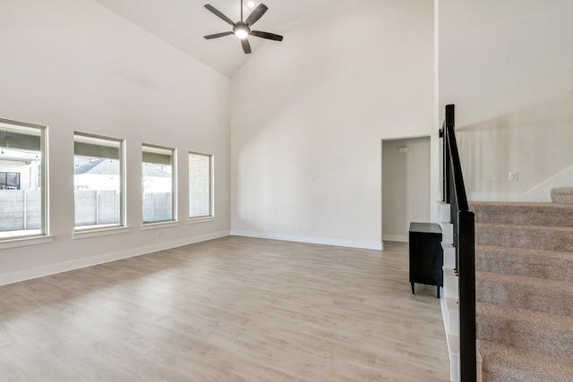 unfurnished living room featuring stairs, light wood-style flooring, baseboards, and ceiling fan