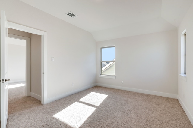 empty room with visible vents, baseboards, light colored carpet, and vaulted ceiling