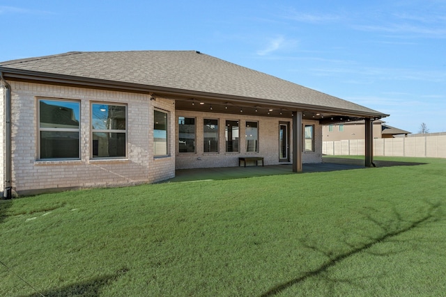 rear view of property with a patio, fence, a yard, a shingled roof, and brick siding