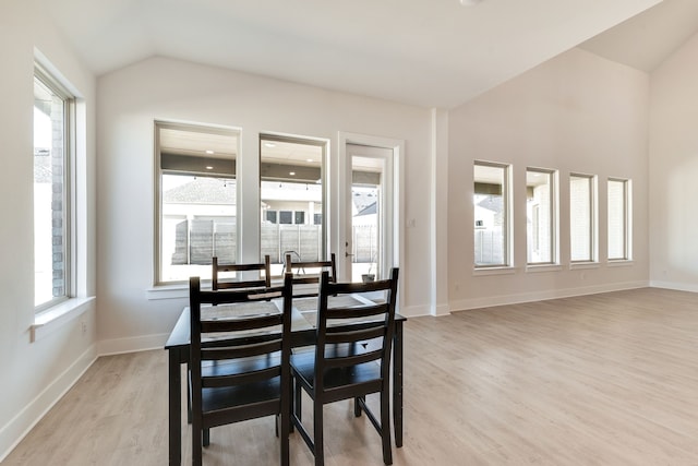 dining room featuring baseboards, lofted ceiling, a healthy amount of sunlight, and light wood-style flooring