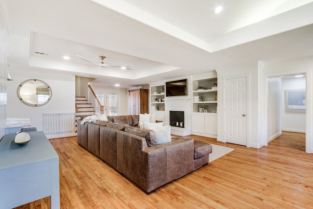 living area featuring radiator, a tray ceiling, light wood-style flooring, a fireplace, and stairs