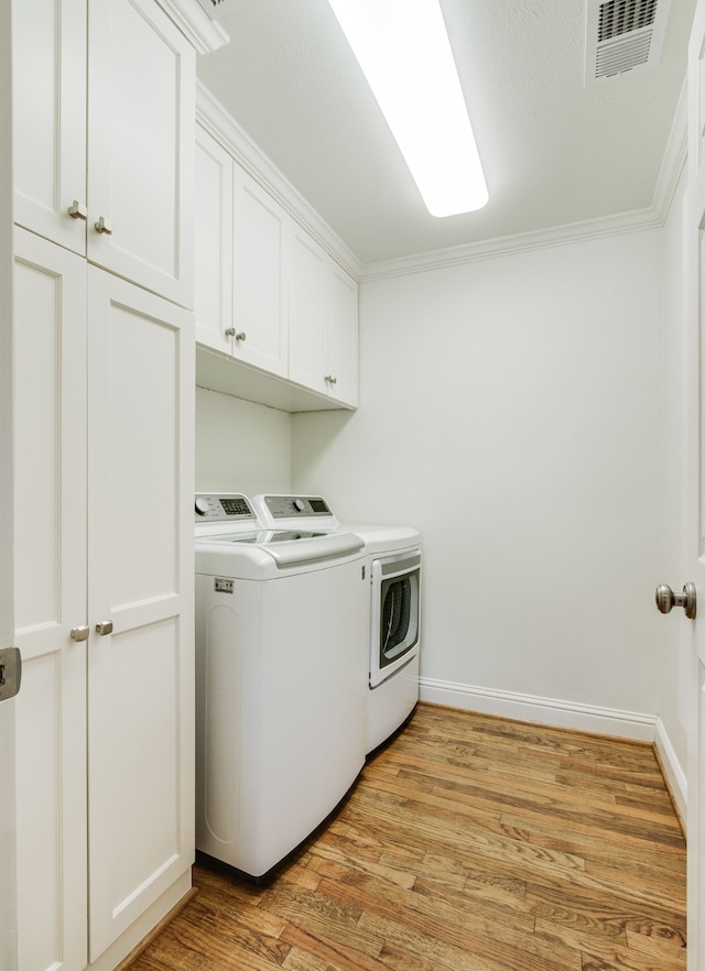 clothes washing area with visible vents, washing machine and clothes dryer, cabinet space, ornamental molding, and light wood-style floors