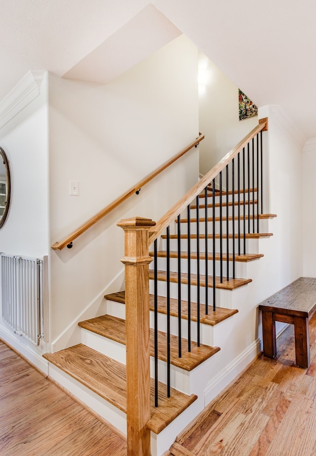 stairway with ornamental molding, radiator heating unit, baseboards, and wood finished floors