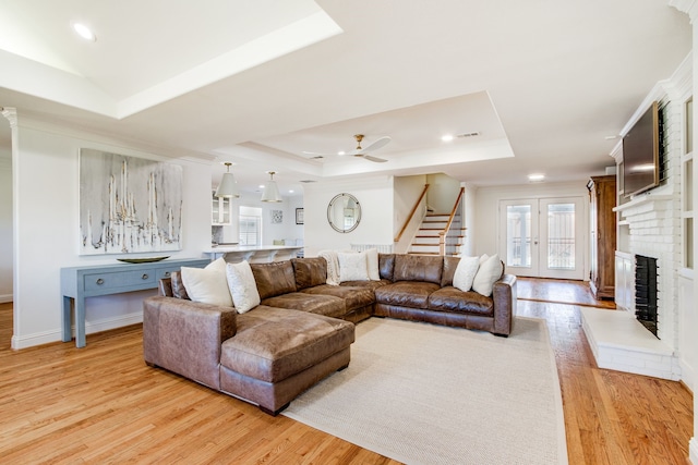 living room featuring light wood finished floors, stairway, a fireplace, a raised ceiling, and a ceiling fan