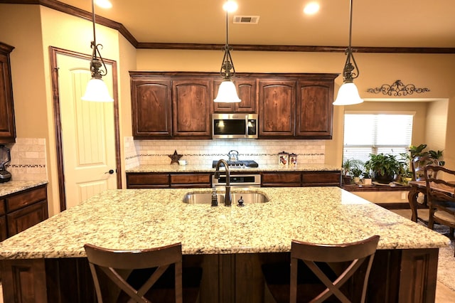 kitchen with a kitchen bar, visible vents, ornamental molding, a sink, and stainless steel microwave