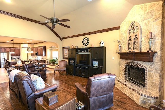 living room featuring ornamental molding, dark wood finished floors, arched walkways, a stone fireplace, and ceiling fan