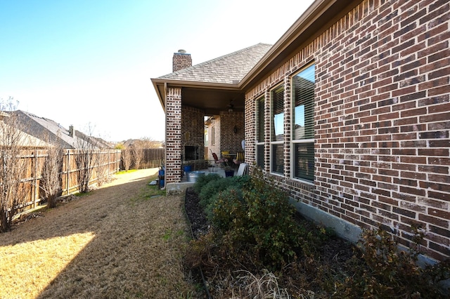 view of side of property with brick siding, a chimney, a yard, a fenced backyard, and a patio