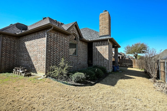 view of side of home featuring brick siding, fence, roof with shingles, a lawn, and a chimney