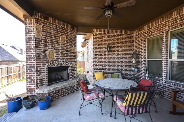 view of patio with a ceiling fan, outdoor dining area, an outdoor brick fireplace, and fence