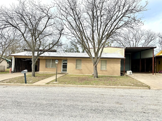 ranch-style house featuring an attached carport, a front yard, driveway, brick siding, and metal roof