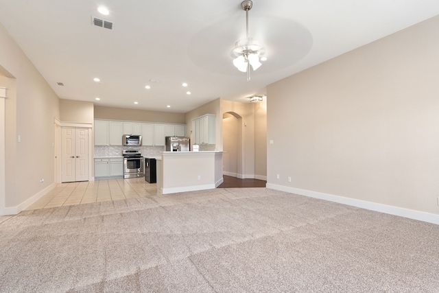 unfurnished living room with recessed lighting, arched walkways, baseboards, light colored carpet, and ceiling fan