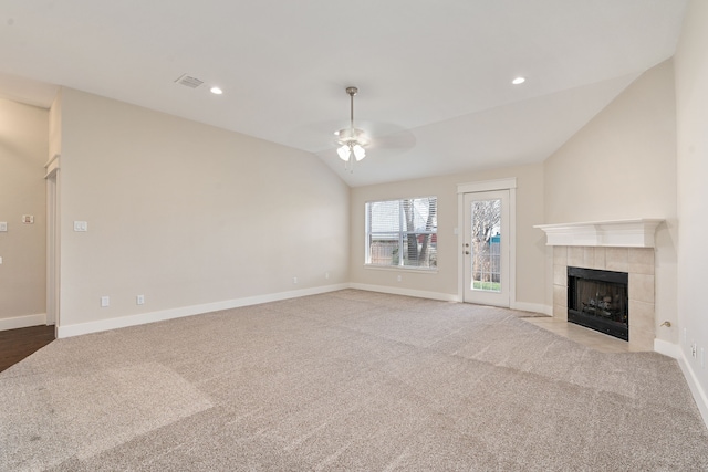 unfurnished living room featuring visible vents, a tiled fireplace, carpet floors, vaulted ceiling, and a ceiling fan