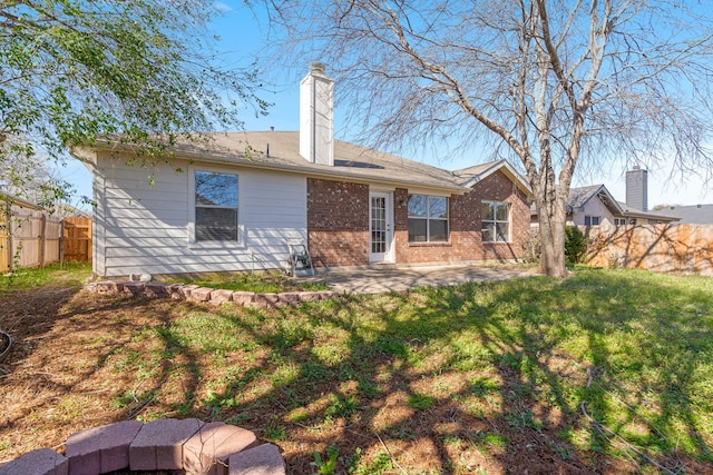 back of house featuring a patio, fence, a yard, brick siding, and a chimney