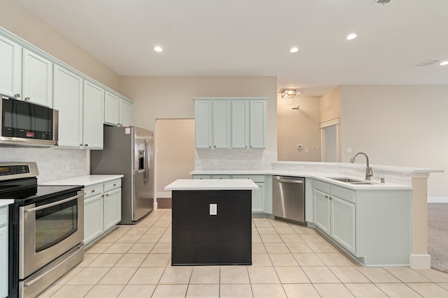 kitchen with a peninsula, a sink, light countertops, appliances with stainless steel finishes, and a center island