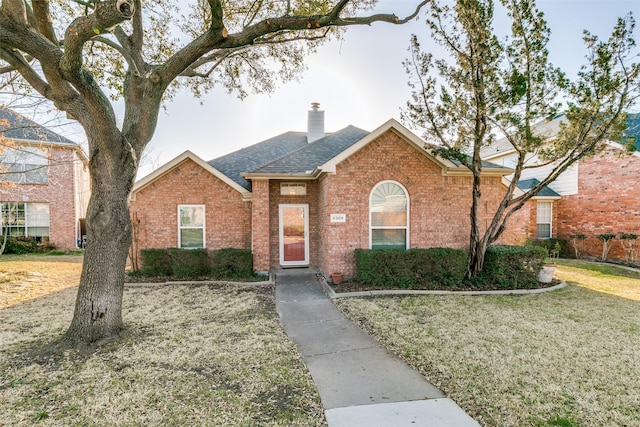 single story home featuring brick siding, a chimney, a front lawn, and a shingled roof