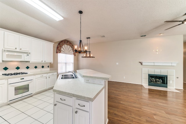 kitchen featuring open floor plan, an island with sink, decorative backsplash, a fireplace, and white appliances