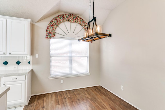 unfurnished dining area with vaulted ceiling, wood finished floors, and baseboards