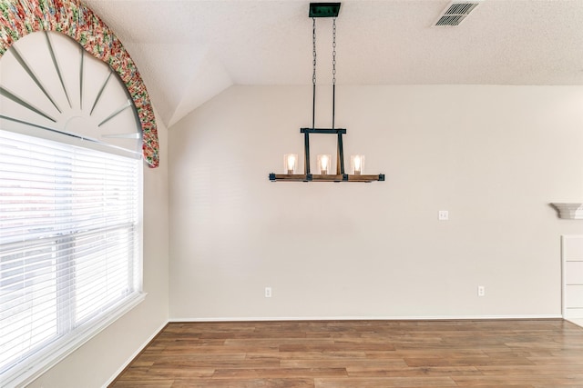 unfurnished dining area with visible vents, wood finished floors, baseboards, a chandelier, and vaulted ceiling