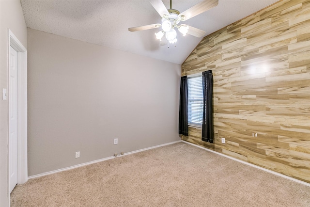 empty room featuring a textured ceiling, carpet, wood walls, ceiling fan, and vaulted ceiling