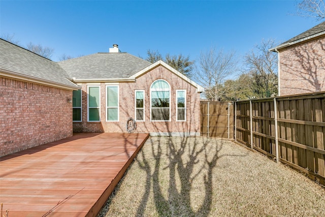 exterior space with a wooden deck, fence, brick siding, and a shingled roof