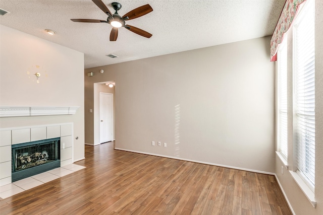 unfurnished living room with a wealth of natural light, a textured ceiling, wood finished floors, and a tile fireplace