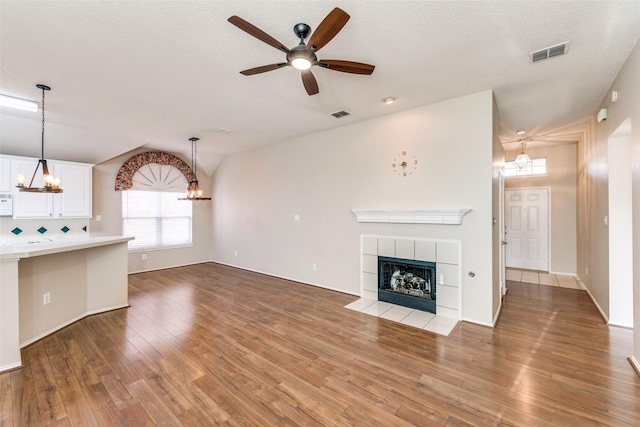 unfurnished living room with a tiled fireplace, light wood-style flooring, ceiling fan with notable chandelier, and visible vents