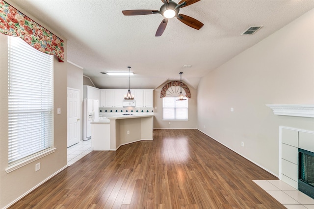 unfurnished living room featuring hardwood / wood-style floors, visible vents, a fireplace, a textured ceiling, and ceiling fan with notable chandelier