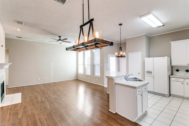 kitchen featuring visible vents, a fireplace with flush hearth, light countertops, white refrigerator with ice dispenser, and a sink