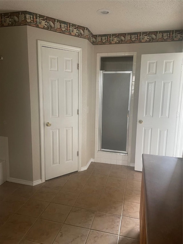 hallway featuring baseboards, a textured ceiling, and dark tile patterned flooring