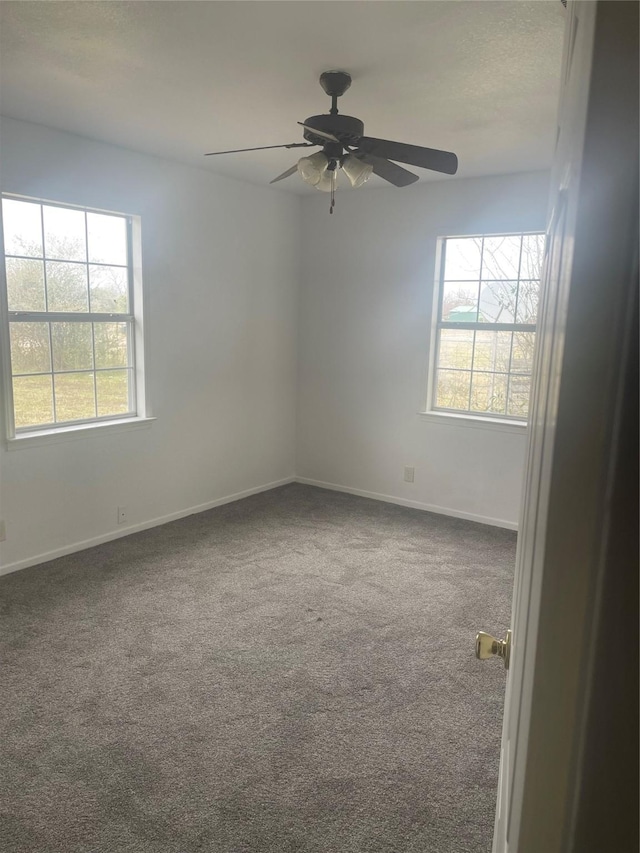 carpeted empty room featuring a ceiling fan, baseboards, and a wealth of natural light