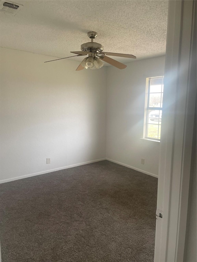 empty room with visible vents, baseboards, ceiling fan, dark carpet, and a textured ceiling