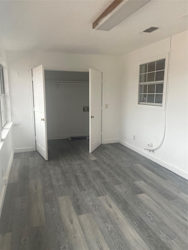 unfurnished bedroom featuring visible vents, baseboards, a closet, a textured ceiling, and dark wood-style flooring