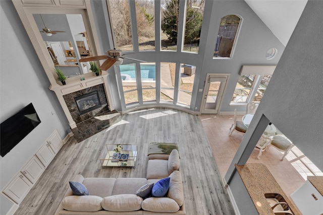 living area with a high end fireplace, wood finished floors, a healthy amount of sunlight, and a towering ceiling