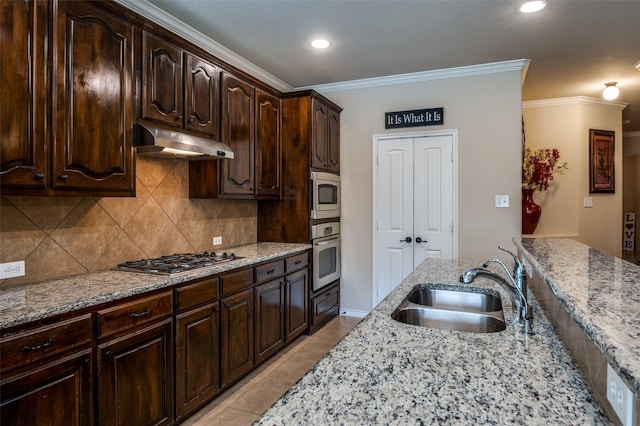 kitchen with ornamental molding, under cabinet range hood, a sink, appliances with stainless steel finishes, and light stone countertops