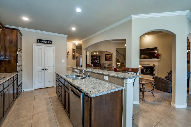 kitchen featuring light tile patterned flooring, a fireplace with raised hearth, a sink, dark brown cabinets, and appliances with stainless steel finishes