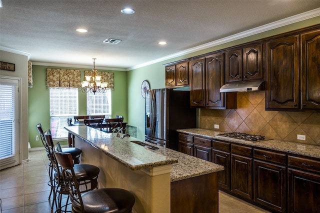 kitchen featuring visible vents, black fridge, under cabinet range hood, a breakfast bar area, and stainless steel gas cooktop