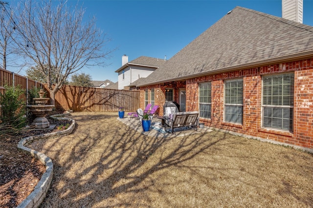 rear view of property featuring a fenced backyard, roof with shingles, brick siding, a chimney, and a patio area