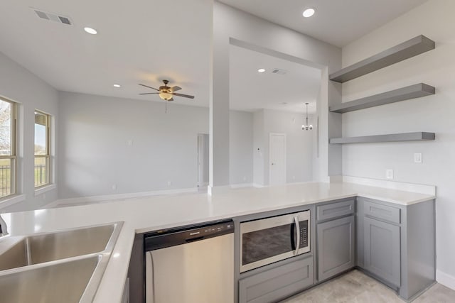 kitchen with visible vents, gray cabinets, ceiling fan with notable chandelier, stainless steel appliances, and a sink