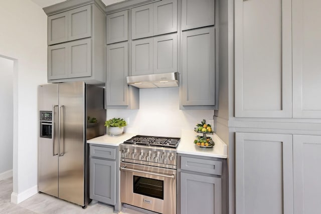 kitchen with under cabinet range hood, appliances with stainless steel finishes, gray cabinets, and light countertops