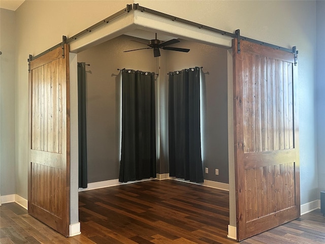 unfurnished bedroom featuring a barn door, baseboards, and wood finished floors